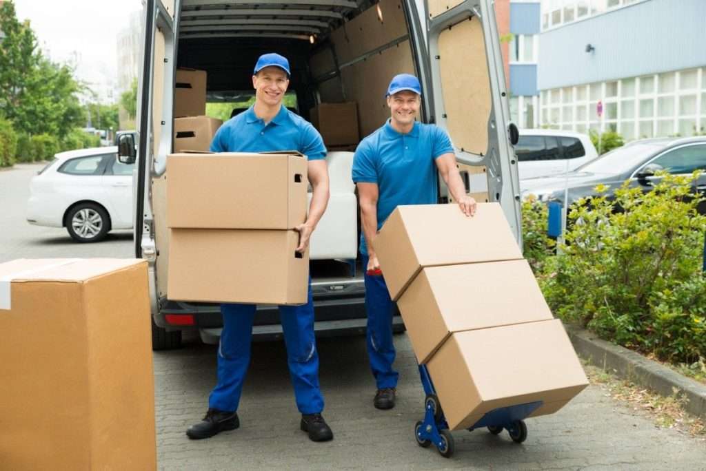 Two smiling Anthem movers in blue polo shirts transporting boxes out of a white van