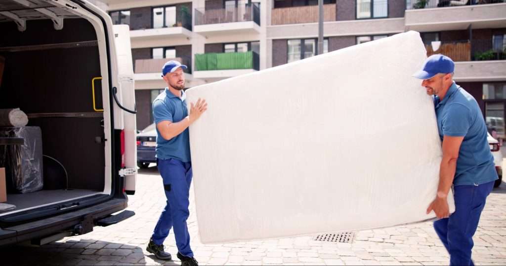 Two movers carrying a mattress out of a moving van.
