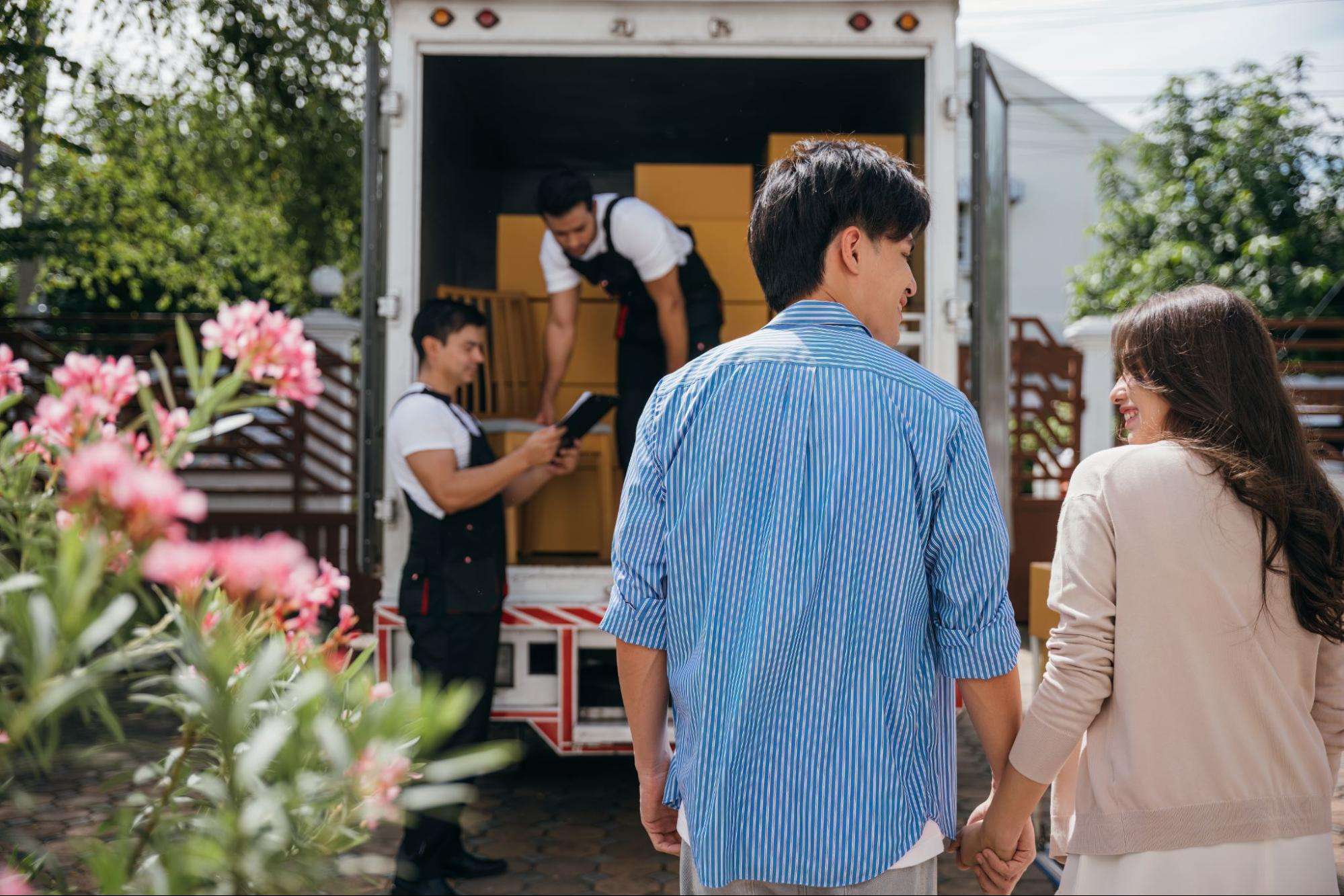 Young couple holding hands and watching Phoenix to Tucson movers load their belongings into a moving truck