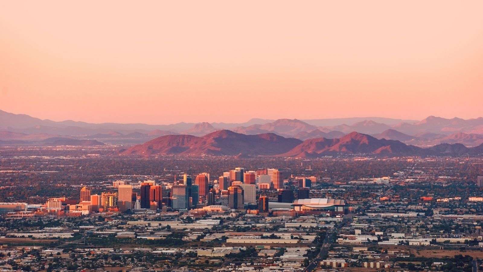 Downtown Phoenix skyline at sunset with colorful townhomes in the foreground and mountain ranges in the background.