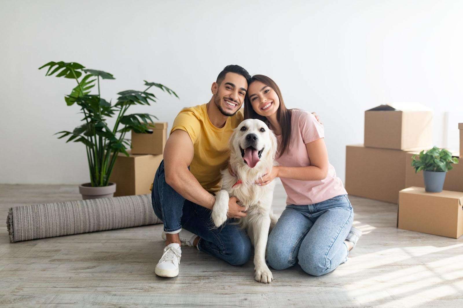 Young couple and dog smiling surrounded by moving boxes