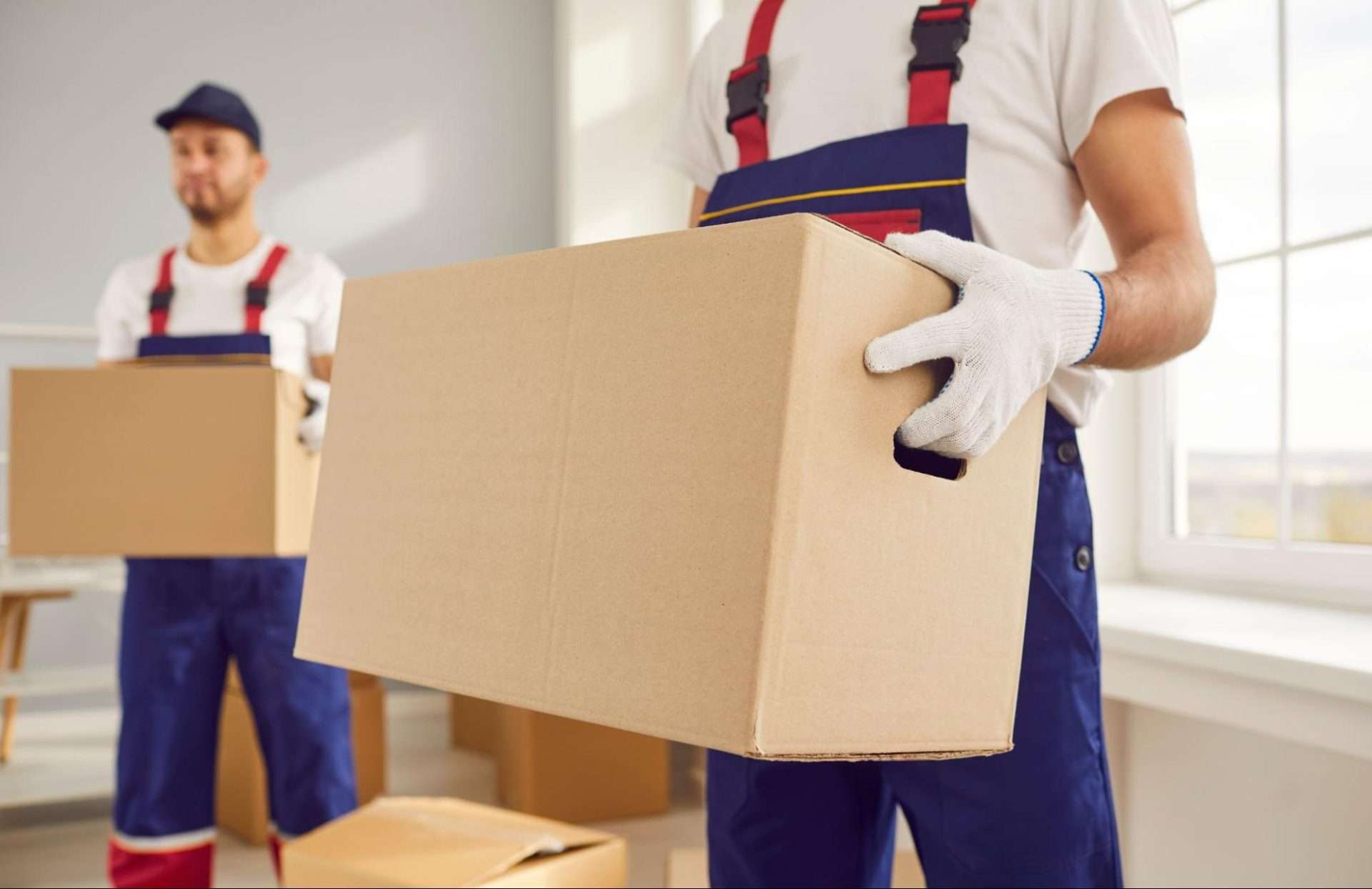 Close up shot of two Phoenix long distance movers in blue overalls and white gloves holding boxes