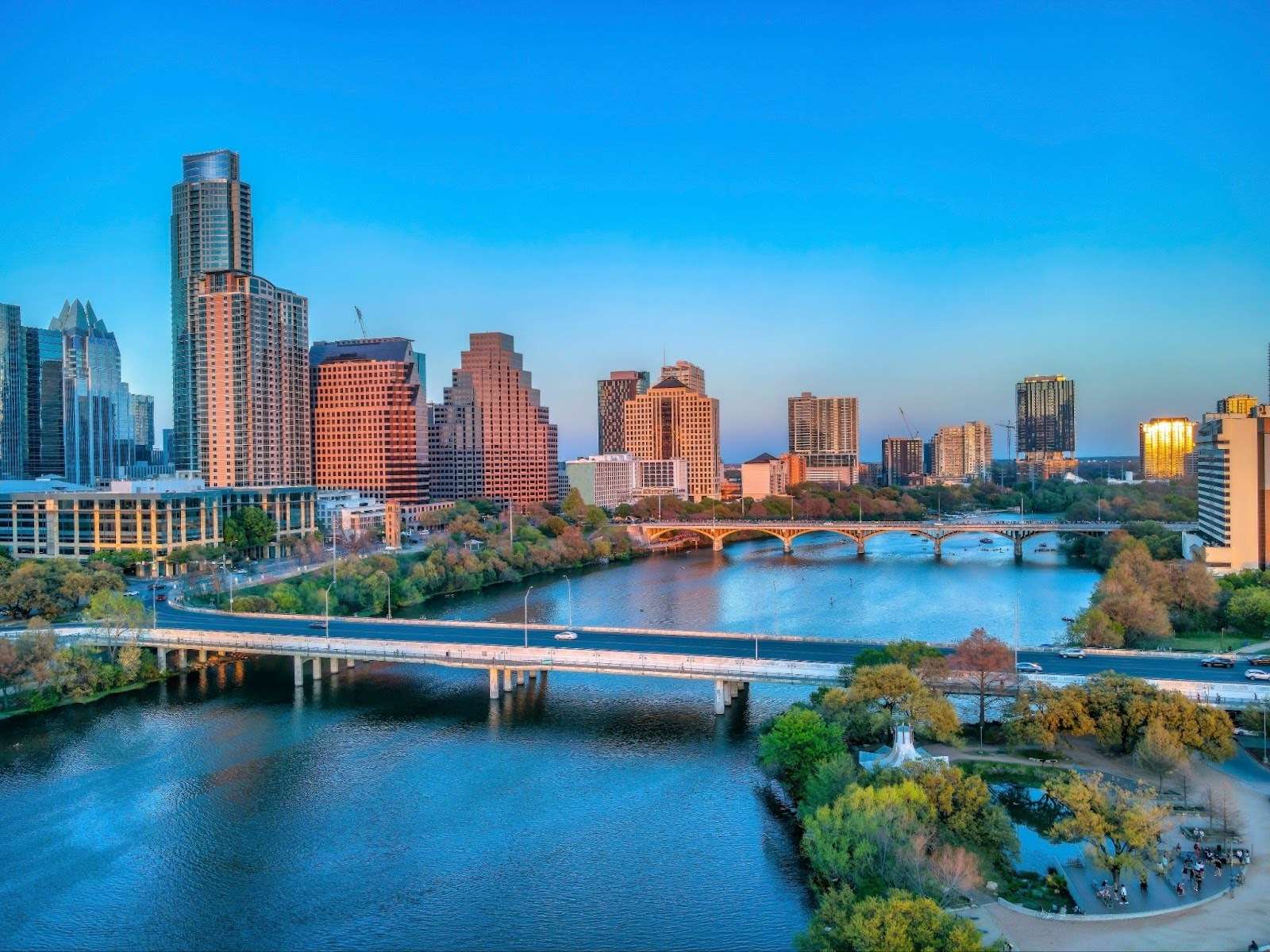 Park and bridges over the Colorado River near the Austin, Texas cityscape during sunset.