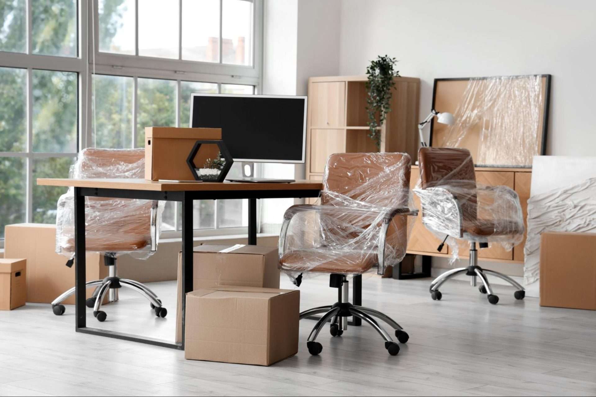 Office furniture in an office wrapped in plastic wrap with various moving boxes scattered around