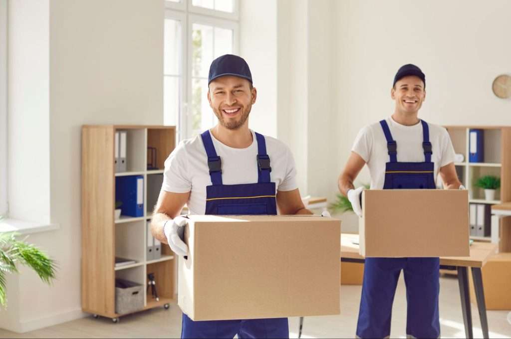 two movers in blue overalls holding boxes and smiling
