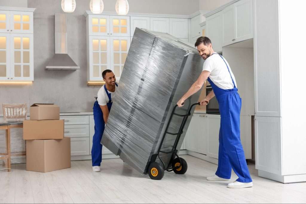 two movers wheeling a plastic-wrapped refrigerator into a kitchen