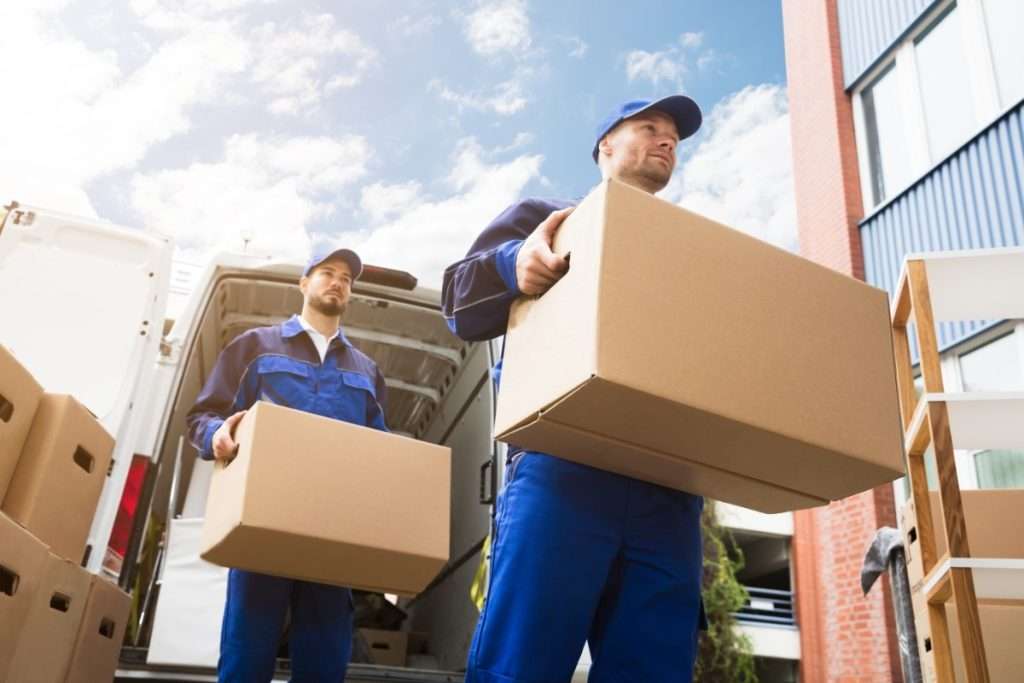 Two Tonto National Forest movers in blue jumpsuit carrying boxes into a customer’s home from the back of a van