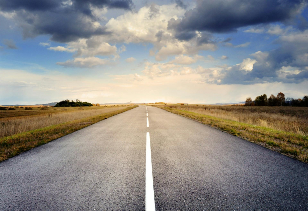 Empty road leading into the sunset, with grass fields on either side.