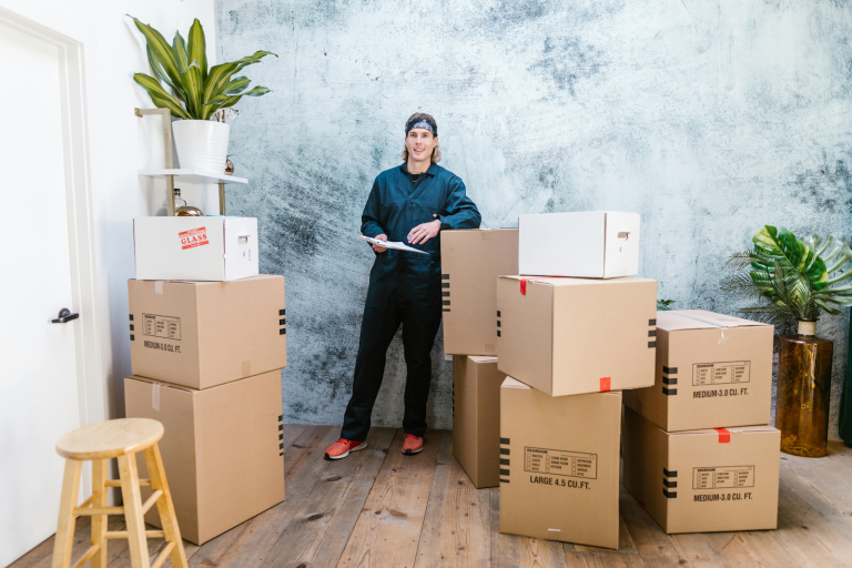 Mover with clipboard smiling, surrounded by boxes.